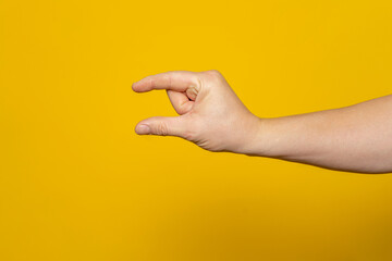 Sturdy man's hand making the small amount gesture isolated on yellow background.