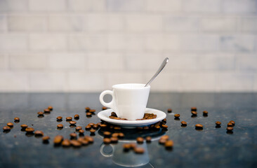 Espresso cup and saucer with spoon and dark roasted coffee beans with modern counter and white subway tile in cafe bar kitchen
