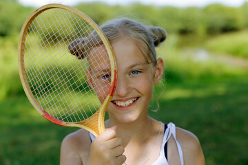 Blonde girl with a badminton racket on a green background. Active rest in summer.