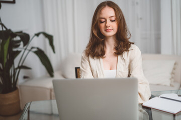 Portrait of a young caucasian woman sitting at the desk with a laptop, typing an email, messaging friend, chatting, dating online with a pleasant smile, long-distance relationships concept