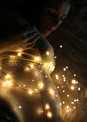Night lamp, yellow garlands. Many light bulbs illuminate the belly of a pregnant woman.