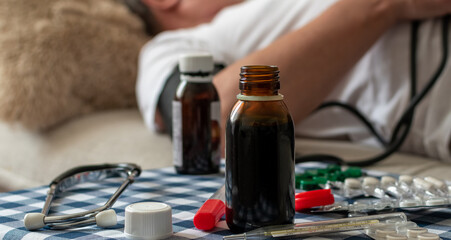 Phonendoscope, thermometer, potions and pills on blurred background of man on sofa at home