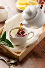 Black tea, pouring tea from tea pot in a white, ceramic cup. Wooden, rustic background
