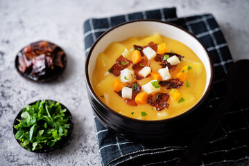 Potato carrot soup with fried bacon slices in a bowl