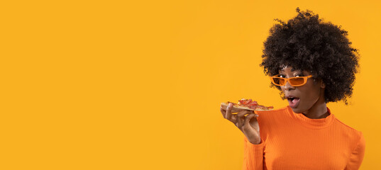 Happy African female with slice of pizza on isolated yellow background.