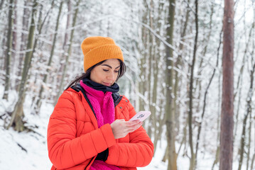 Fototapeta na wymiar Young Woman using mobile phone in the Snowy Winter Mountain .Woman using trail map in the forest 