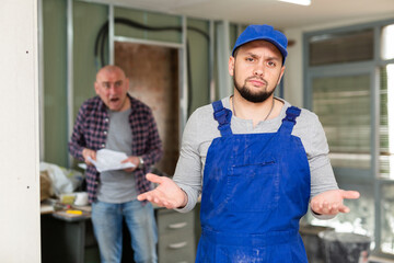 Repairman confused by angry owner of apartment who standing behind and shouting.
