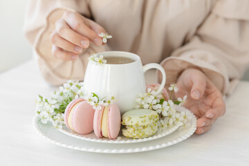 Traditional delicious French dessert - sweet homemade macarons on a vintage plate. Colourful tasty macaroons served on a white china with herbal tea. Decorated with fragile cherry tree flowers.
