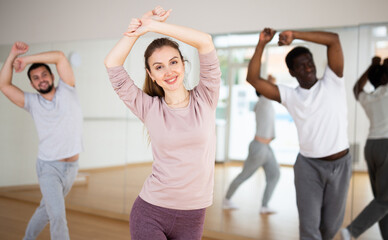 Energetic sporty young woman practicing modern vigorous dance movements in group dance class ..