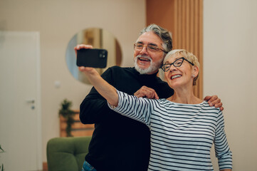 Senior couple using smartphone together at home and taking a selfie