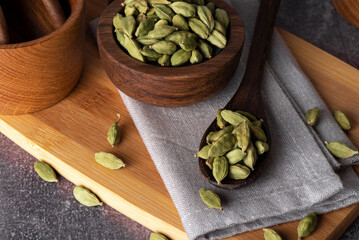 Green cardamom in wooden bowl and spoon. Dry cardamom spice. Cardamom seeds macro shot.
