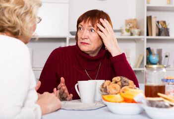 Upset mature lady having unpleasant talk with female friend at home