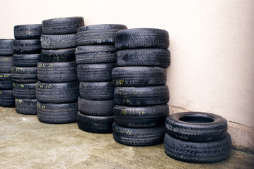 Stacks of various car new and used tires along a wall in an outdoor warehouse. Sale of used tires, recycling