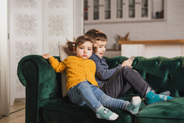 Obraz premium Kids sitting on sofa and using mobile device for playing games or have a videochat