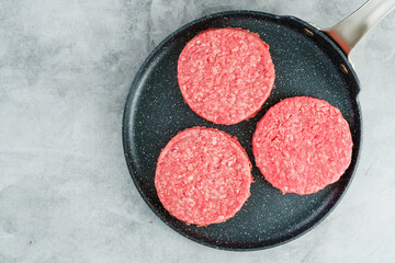 Burger patties close-up. Fresh raw burger patties close-up on a frying pan on a grey stone background, flat lay