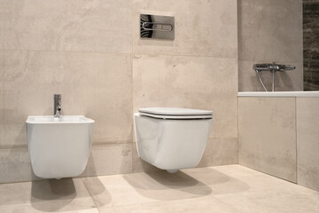 Fototapeta na wymiar White wall-hung bidet and toilet, on gray ceramic tiles in bathroom