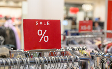 Red sale sign in retail store with clothes on hangers