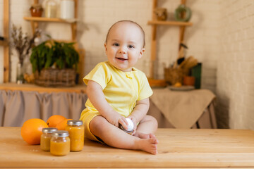 a cute kid in a yellow bodysuit is sitting in the kitchen with cans of baby food. The first complementary feeding of the child. Baby purees