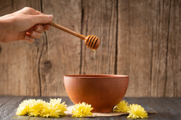 Honey is poured from a dipper into a clay bowl on a wooden background.