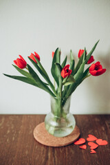 Red tulips flower bouquet in glass vase on table empty copy space.Fresh flowers on wooden background. red paper hearts