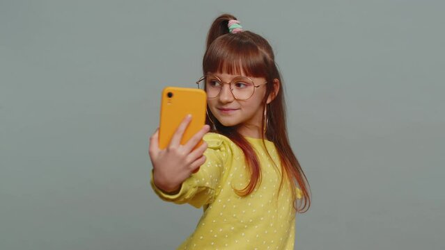 Young preteen child girl kid blogger taking selfie on smartphone holding in hand, communicating video call talking online with subscribers. Little toddler children isolated on studio gray background