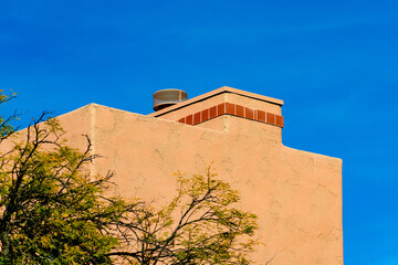 Block style chimney on an adobe house with tiny red tiles or bricks on vent with metal top and front or back yard tree