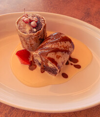 Custard cream egg crepe dessert with berries and chocolate served on a white plate. This is a food closeup.