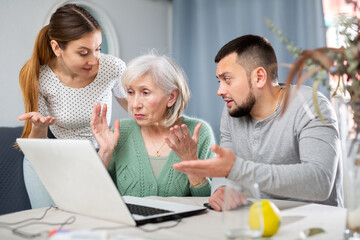 Young adult son and his wife giving help with laptop to stressed elderly mother at home