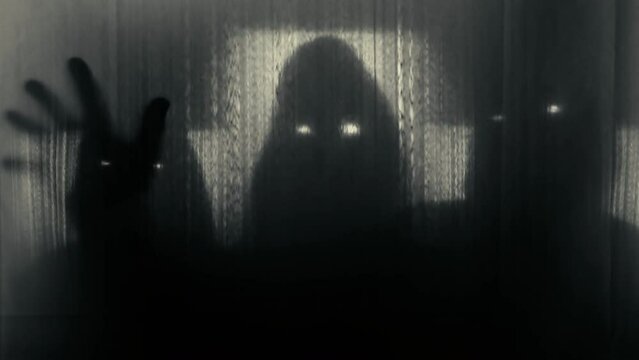 Silhouettes of three people in hoods with glowing eyes behind a transparent curtain, raising their heads and pulling out their hands. Concept of demons, paranormality, ghosts. 4k video 60 fps.