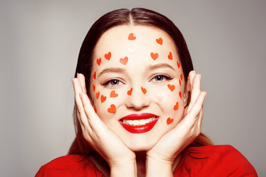 Portrait of a woman with stickers of hearts on her face. The girl is narcissistic, the girl is smiling at the camera, on a gray background. Self-love, skin care, make-up, courses for women.