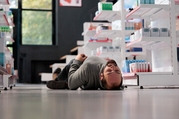 Young caucasian man having epilepsy attack, lying unconscious on floor in medical retail store....
