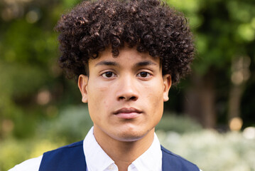 Portrait of biracial groom with curly hair looking to camera in garden