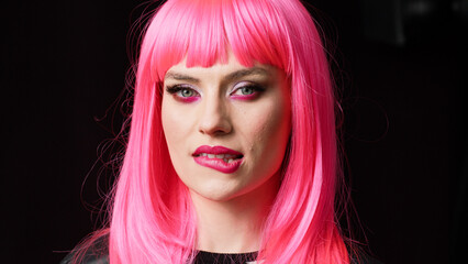 Sexy beautiful woman showing candid smile on camera, feeling happy and positive. Female model smiling and wearing beautiful makeup with pink hair wig, being cheerful and confident.