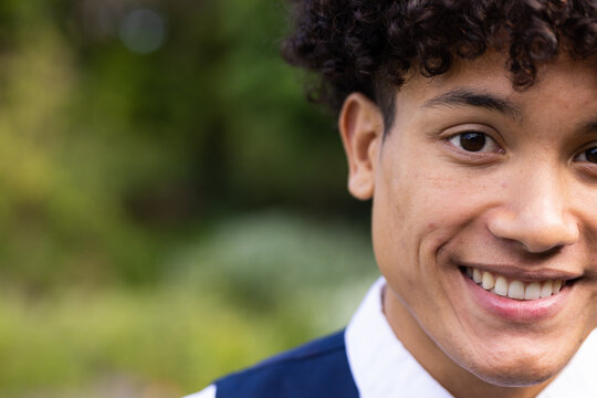Portrait of smiling biracial groom with curly hair in garden at outdoor wedding, with copy space