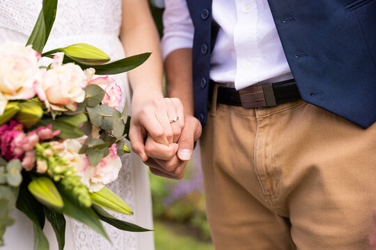 Midsection of diverse bride and groom holding hands and bouquet at outdoor wedding