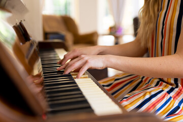 Midsection of caucasian woman playing piano at home