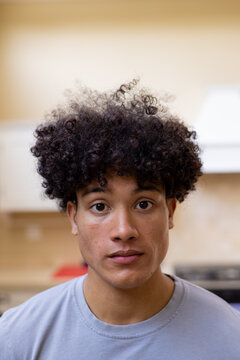 Vertical portrait of biracial man with curly hair in kitchen at home