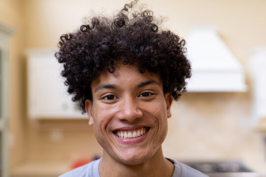 Portrait of smiling biracial man with curly hair in kitchen at home