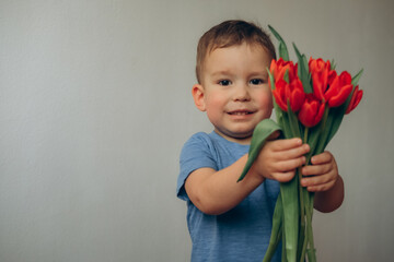 Mothers Day. cute toddler boy with a bouquet of flowers. A bouquet of red tulips in the hands of his son, a little gentleman on a white background.