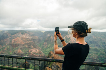 girl taking picture on phone ingirl taking picture on phone in waimea canyon