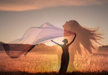 woman in the field feeling free at peace in nature holding fabric cloth blowing in the wind. 