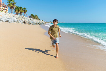 Front view of young boy barefoot running on beach while smiling