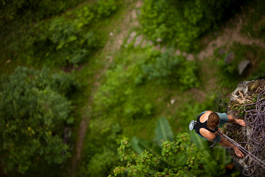 Caucasian female climer looking down from belay station 60 metres above in rural Asia.