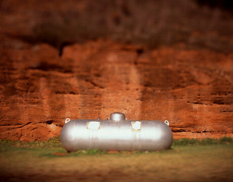 An ordinary silver propane tank with a backdrop of a red rock wall at a camp ground in Oklahoma.