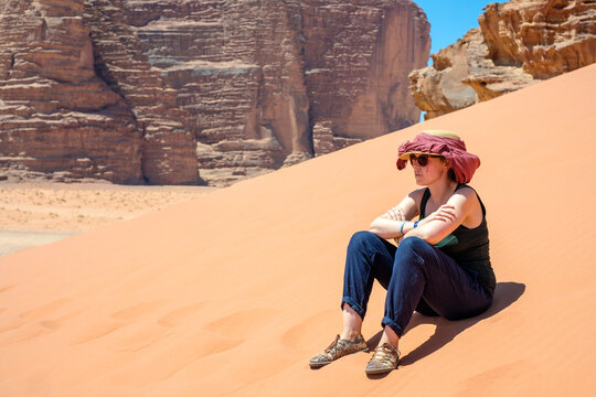 Tourist sits on sand dune in hot sun, Wadi Rum Protected Area, Jordan