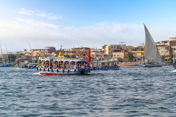 Colorful touristic river cruise boats and feluccas on the African Nile River as they travel through the central district of Luxor, Egypt. - obrazy, fototapety, plakaty