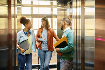 Diverse work colleagues using elevator in modern coworking office - obrazy, fototapety, plakaty