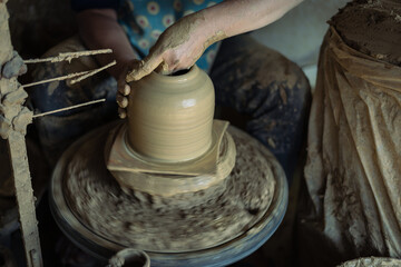 Male hands make sculpt wet clay on a potter's wheel sculpt vessel clay in a fast-moving circle in a clay pot, raw clay shaping, and traditional craft.