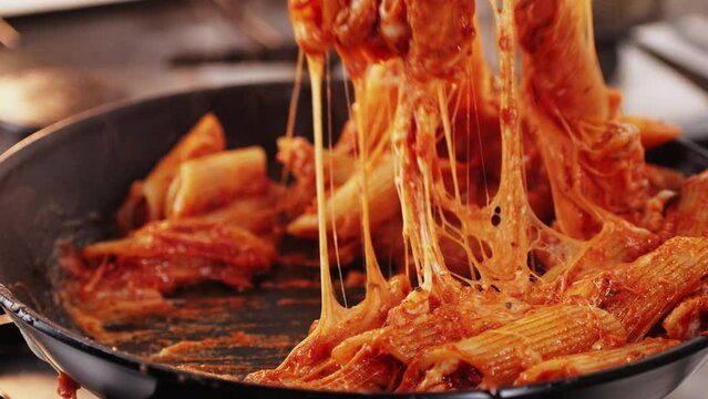 Chef cooking penne pasta with tomato sauce and mozalerra cheese in pan, close up. Cooking traditional italian cuisine, food in Italy.