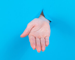Woman stretching her palm through a hole on a blue background. 